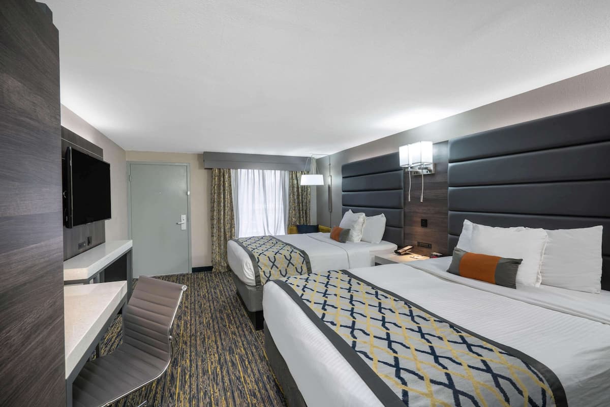 Habitación de hotel con dos camas, un escritorio, una silla, un televisor y una ventana con cortinas.