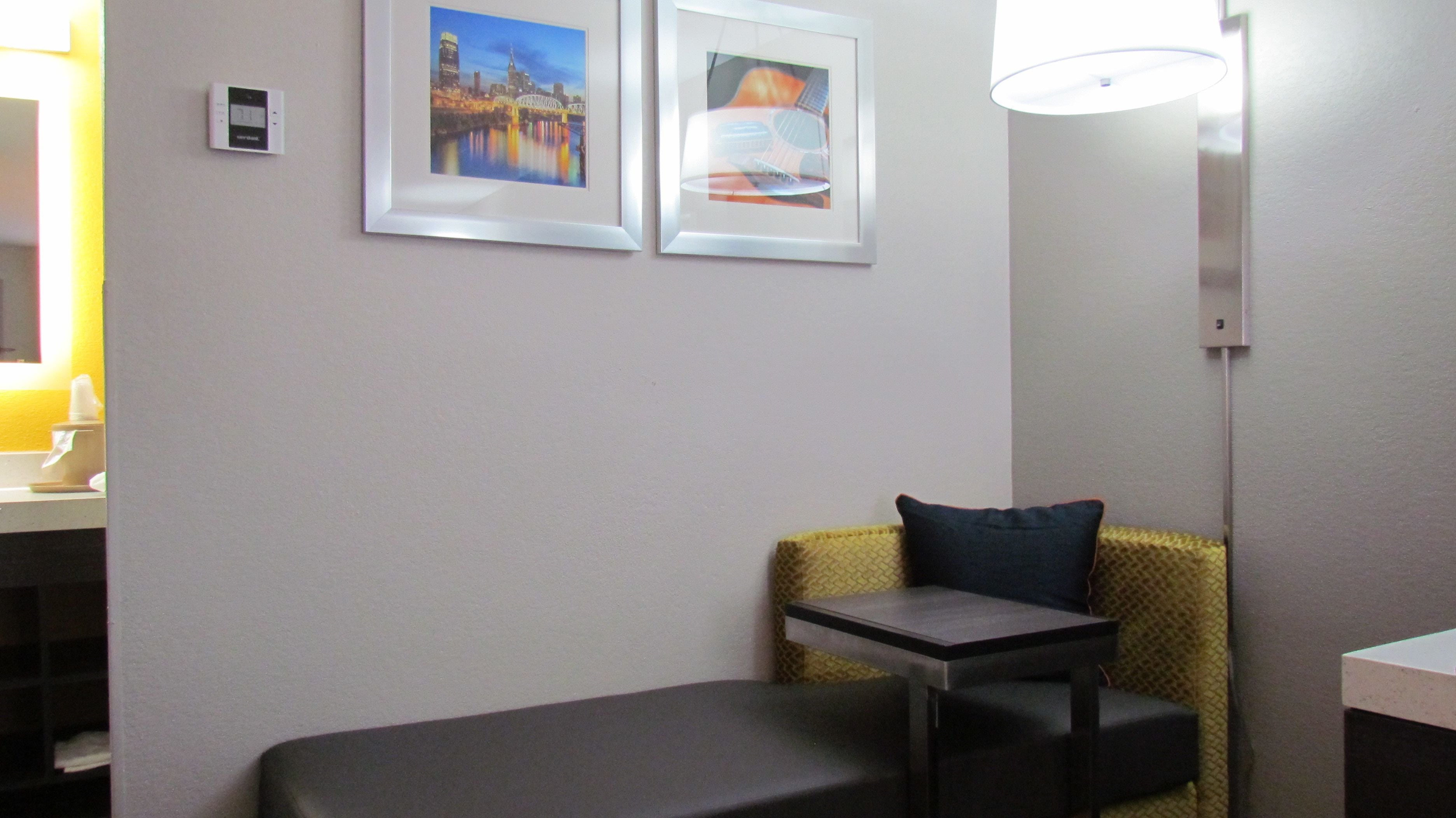 A hotel room with a bed, a small table, a chair, and two framed pictures on the wall.
