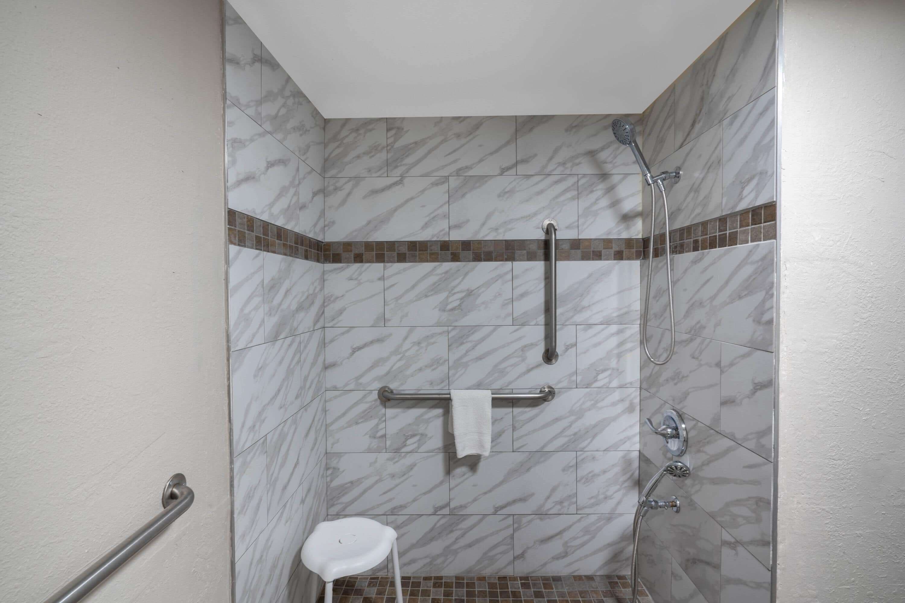 A shower area with a handrail, a grab bar, and a small stool.