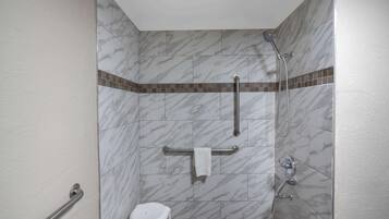 A shower area with a handrail, a grab bar, and a small stool.