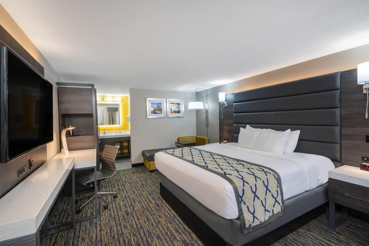 Habitación de hotel con cama, escritorio, silla, televisor, lámpara y mesita de noche.