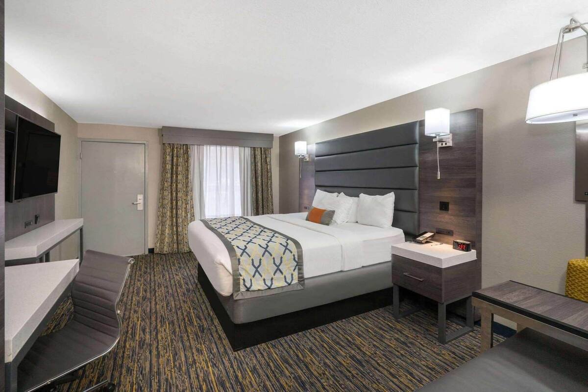 Una habitación de hotel con cama, mesita de noche, lámpara, televisor y un escritorio con silla.
