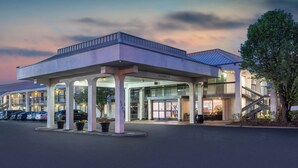 A hotel with a covered entrance, outdoor seating area, and a parking lot.