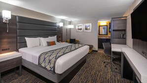 A hotel room with a large bed, a desk, a chair, a TV, and a bathroom visible in the background.