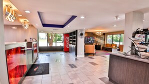 A modern hotel lobby with a reception desk, seating area, and a large Coca-Cola sign.