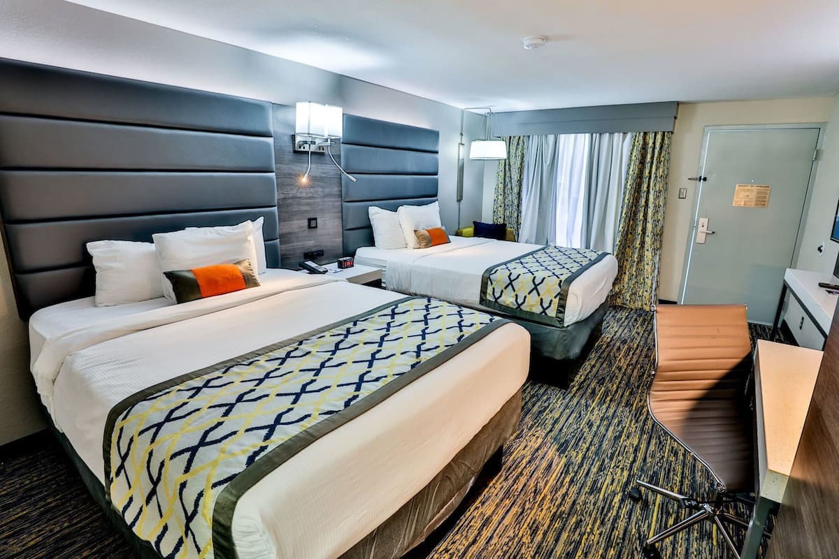 Habitación de hotel con dos camas, un escritorio, una silla, un espejo y una ventana con cortinas.