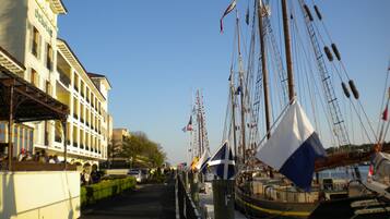 A marina with multiple boats docked, a building with balconies, and a clear sky.