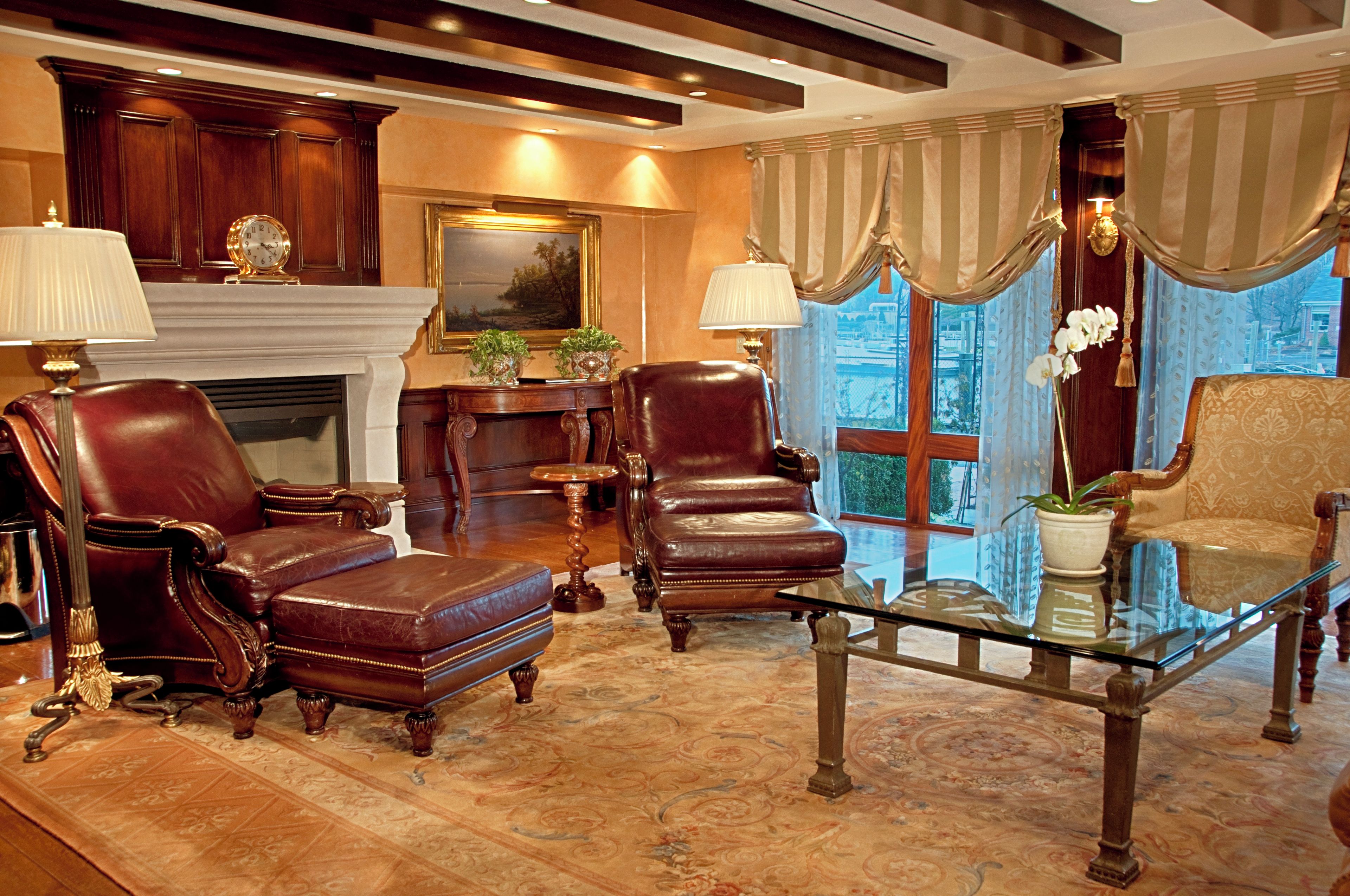 A traditional room with leather chairs, a fireplace, a painting, and a view through a window.
