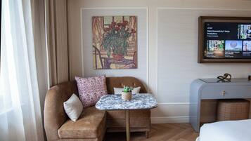 A hotel room with a sofa, a small round table, a television, and a painting on the wall.