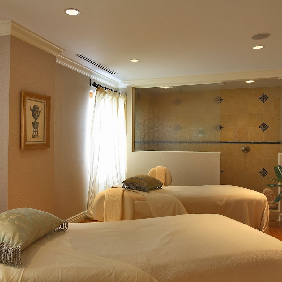 A hotel room with two beds, a large window with curtains, a framed picture on the wall, and a potted plant.