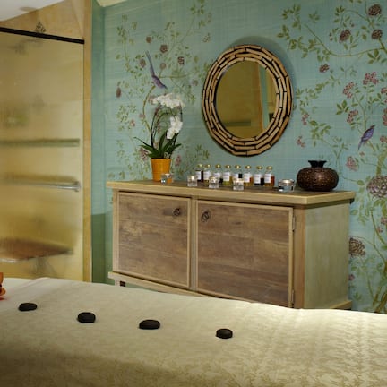 A spa room with a massage table, a wooden cabinet with bottles, and a mirror on the wall.