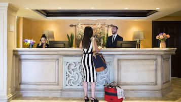 A reception desk with two receptionists, a decorative wall, and a red bag on the floor.