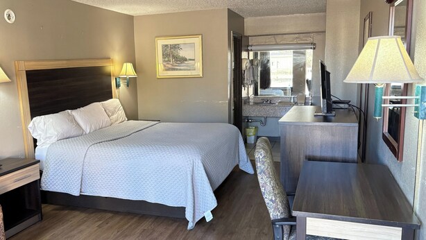 A hotel room with a bed, bedside table, lamp, chair, desk, and a small kitchenette area. - American Inn by Hotel O Selma US 80 (Selma)