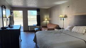 A hotel room with a bed, a desk, a chair, a lamp, and a view of the outside. - American Inn by Hotel O Selma US 80 (Selma)