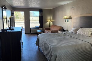 Habitación de hotel con cama, escritorio, silla, lámpara y vistas al exterior.