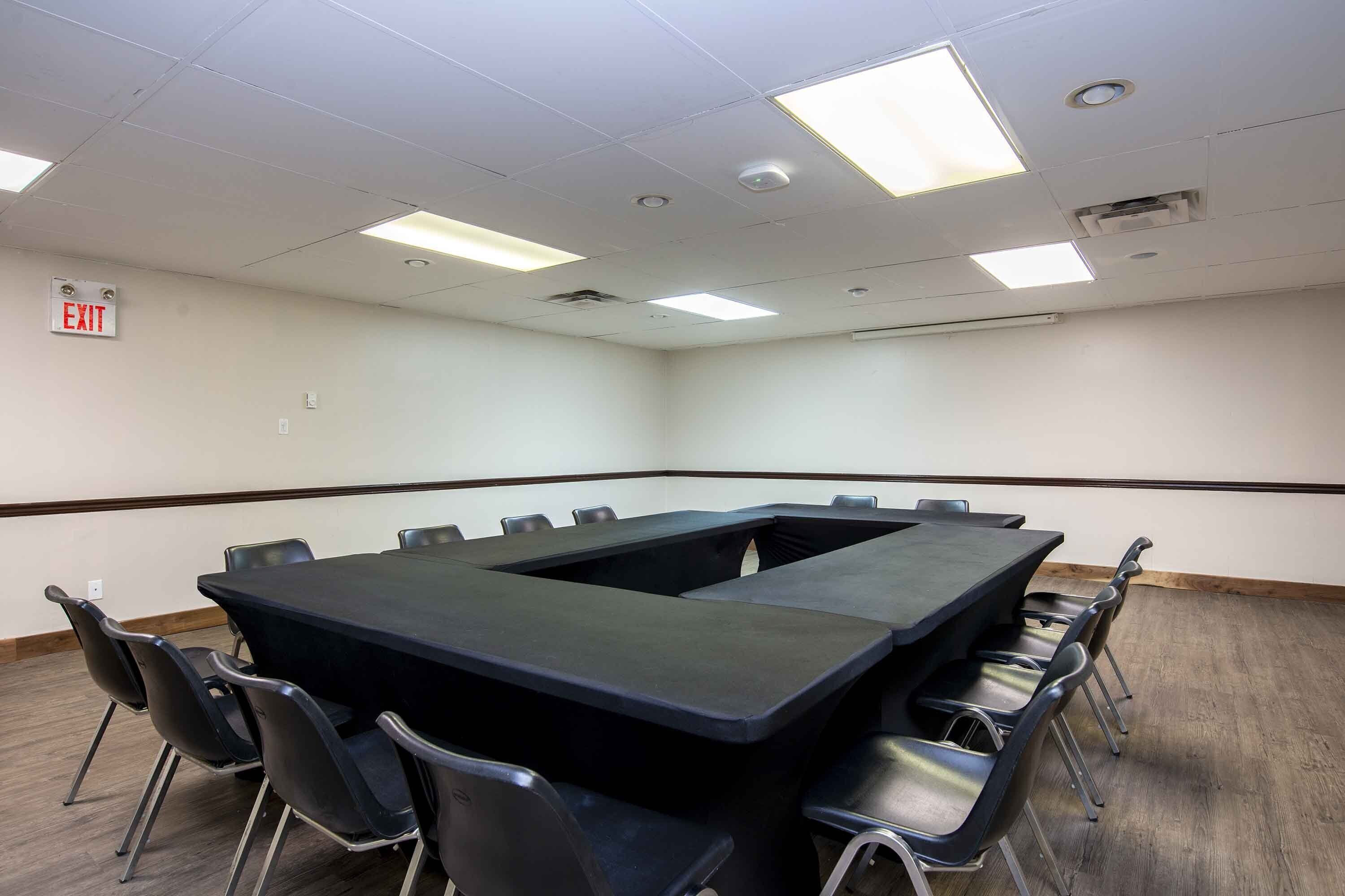 A conference room with a large rectangular table, black chairs, and a white ceiling with fluorescent lights.