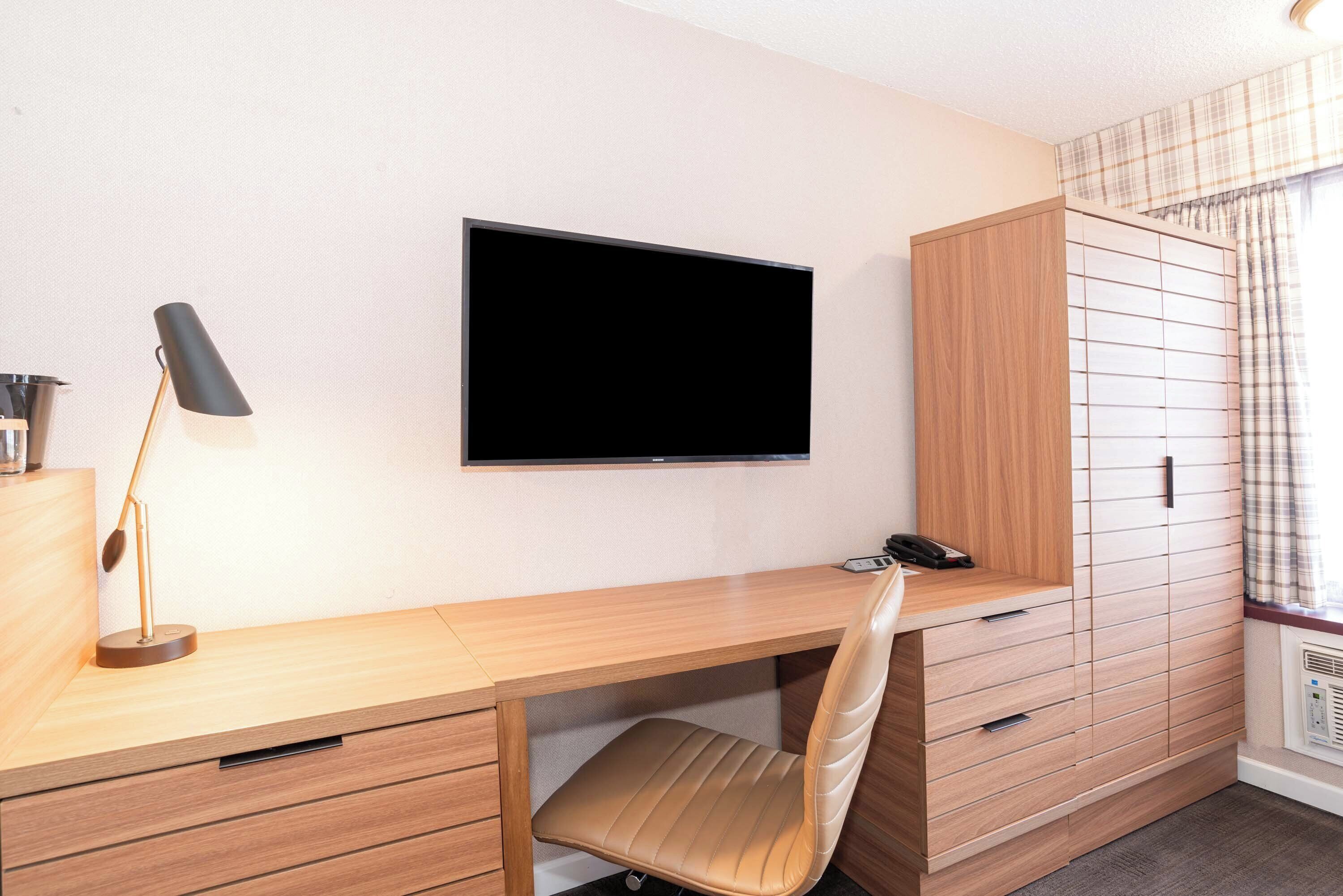 A modern room with a wooden desk, a chair, a television mounted on the wall, and a wardrobe with multiple compartments.