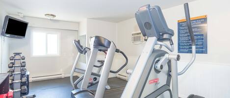 A gym with treadmills, dumbbells, and a TV screen.