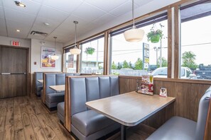 A restaurant interior with booths and tables, wooden flooring, hanging plants, and a view of the street outside. - Sandman Hotel Terrace (Terrace)