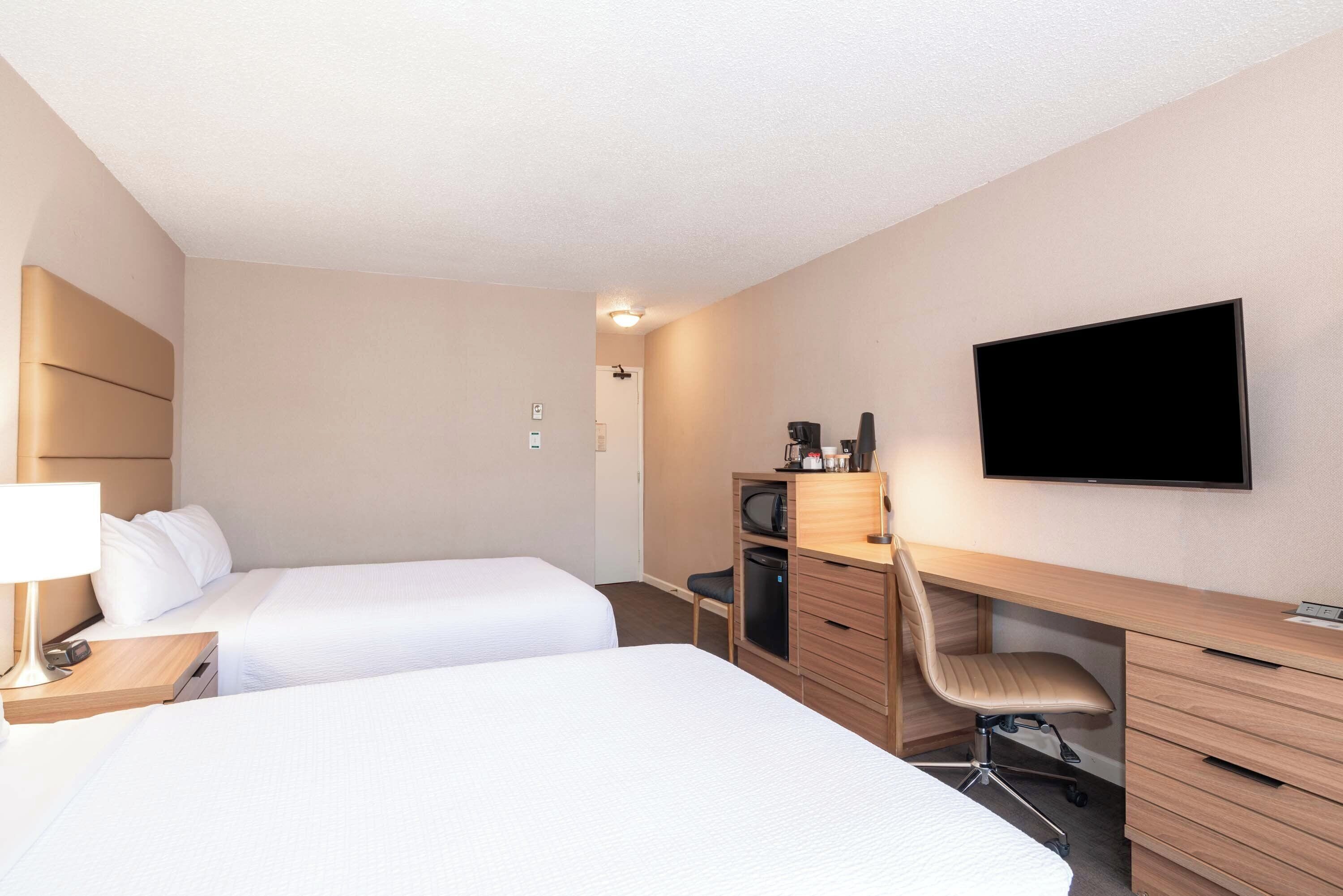 A hotel room with two beds, a desk with a chair, a television, and a minibar.