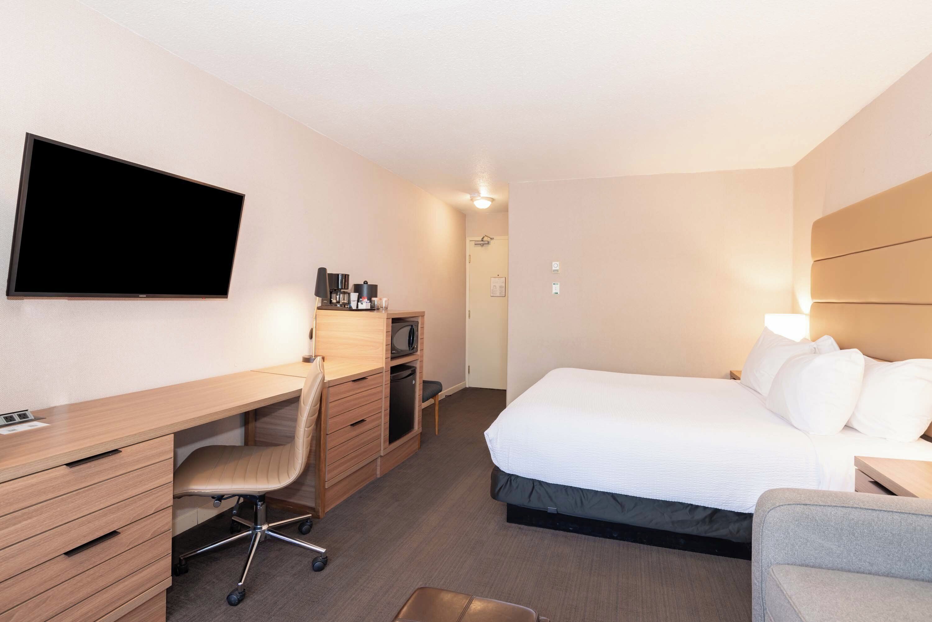 Ein Hotelzimmer mit Bett, Schreibtisch mit Stuhl, Fernseher und Nachttisch.