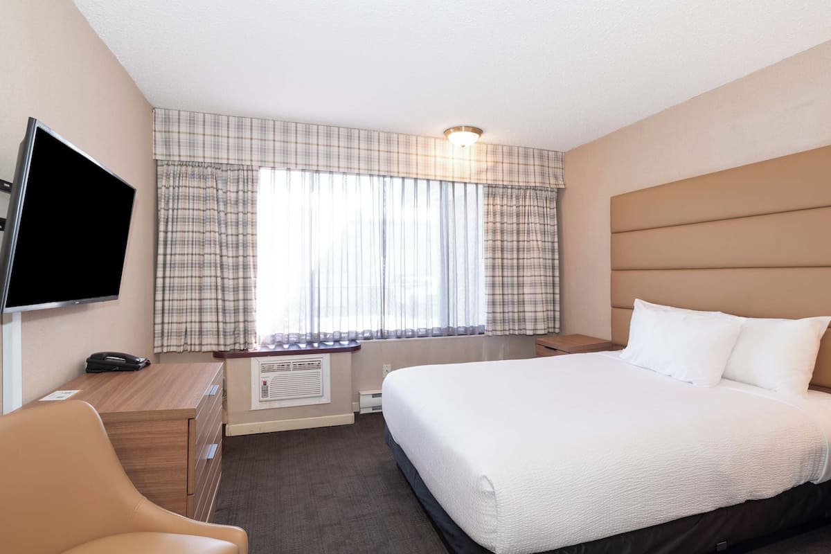 A hotel room with a bed, a desk with a telephone, a television, and a window with curtains.