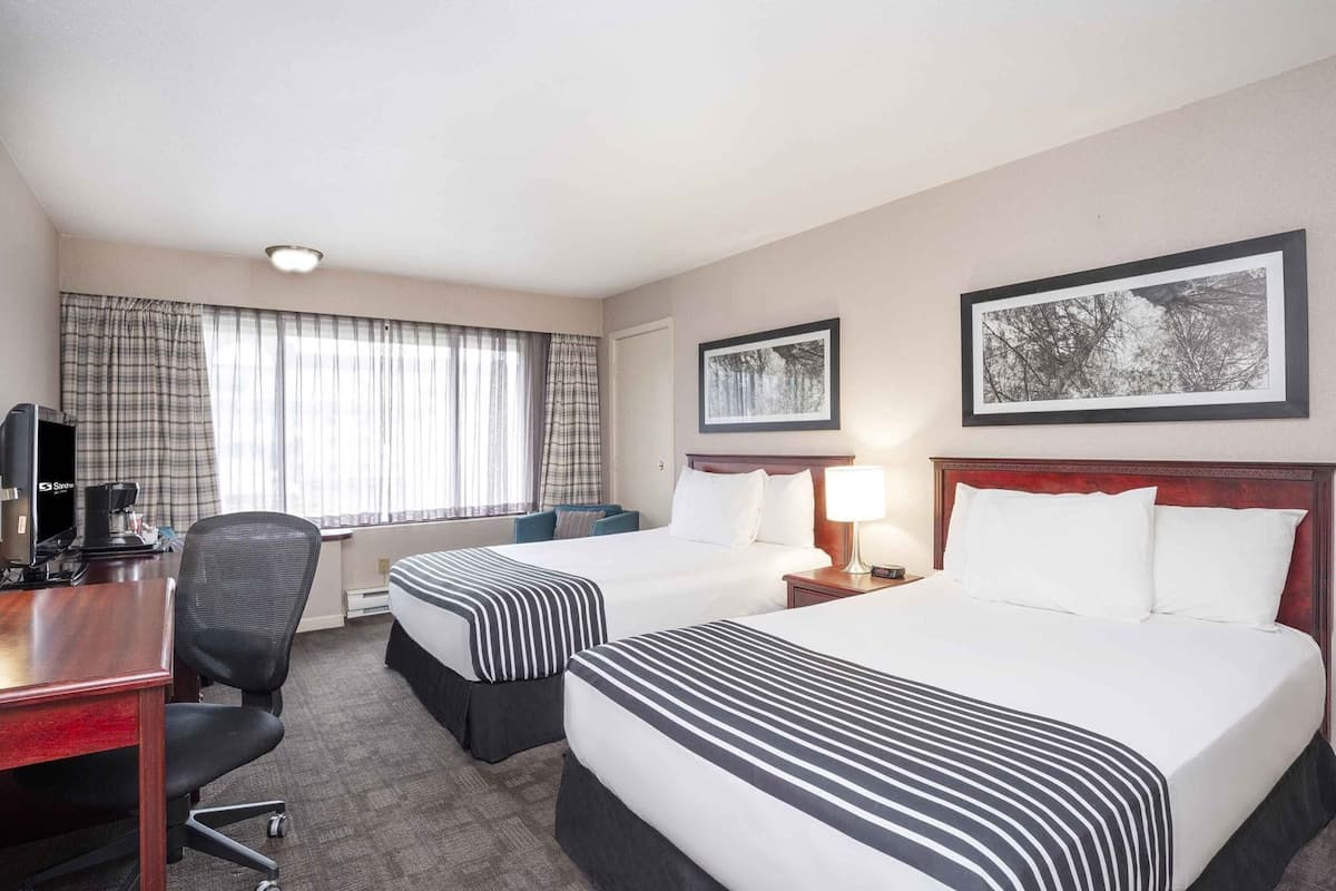 A hotel room with two beds, a desk, a chair, a TV, and two framed pictures on the wall.
