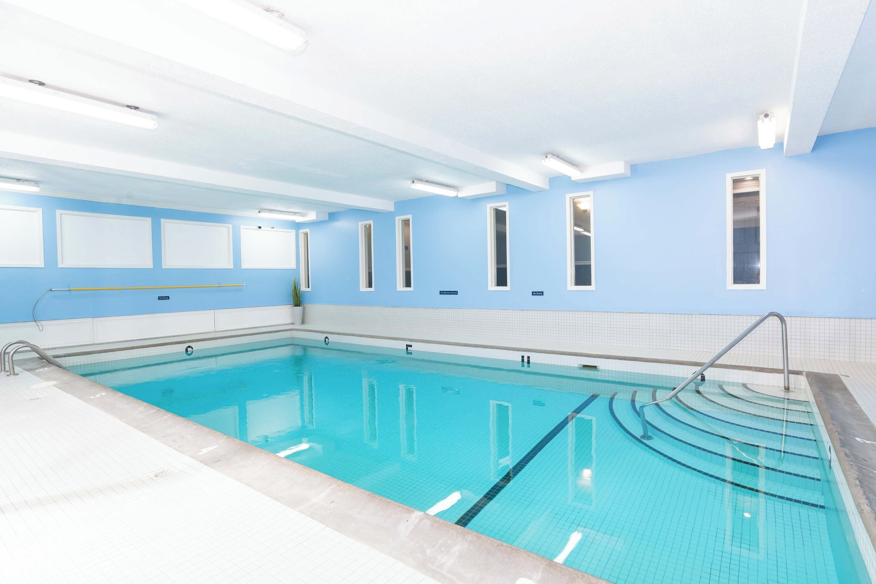 A swimming pool with clear blue water, tiled walls, and a ceiling with fluorescent lights.