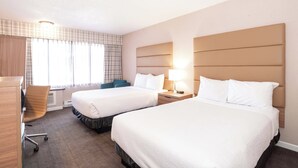 A hotel room with two beds, a desk, a chair, and a window with curtains.