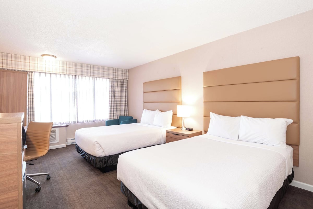 A hotel room with two beds, a desk, a chair, and a window with curtains.