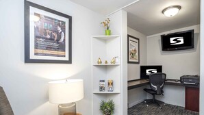 A hotel room with a desk, chair, lamp, bookshelf, and a TV mounted on the wall.