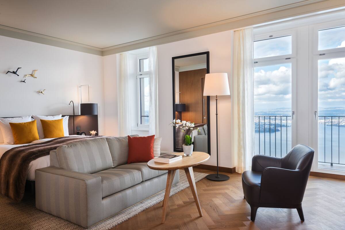 Quarto de hotel moderno com sofá, poltrona e uma mesinha com um livro e um vaso.