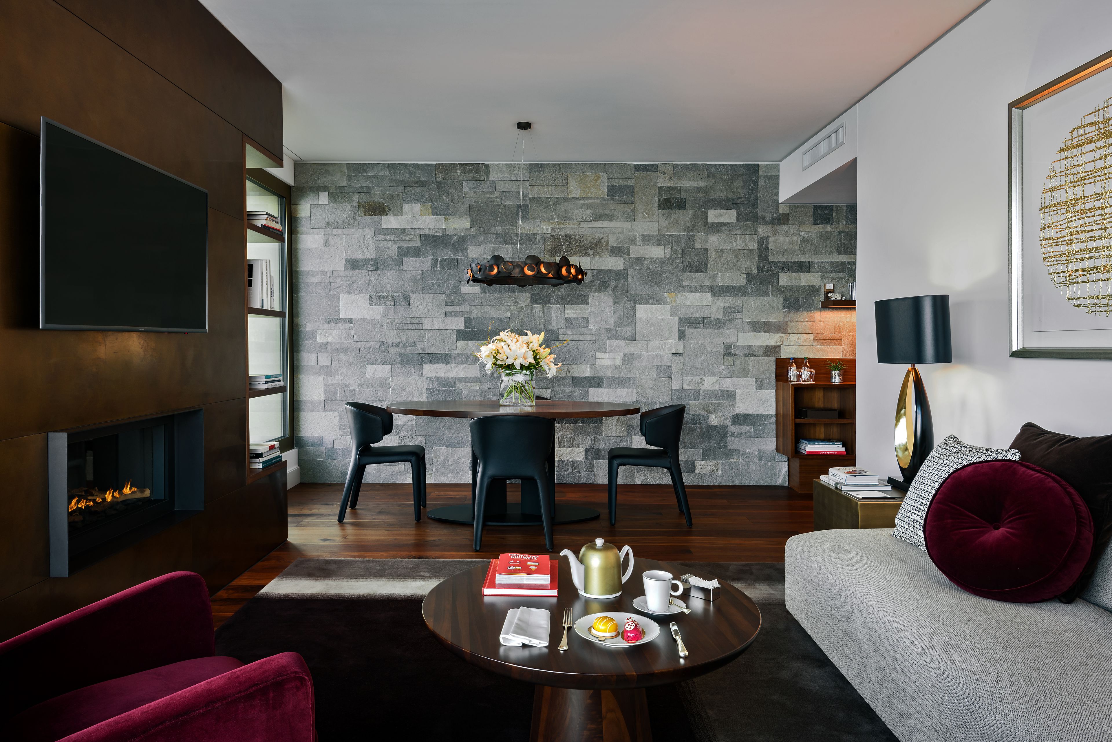 A modern living room with a fireplace, a round dining table, and a sofa with a red cushion.