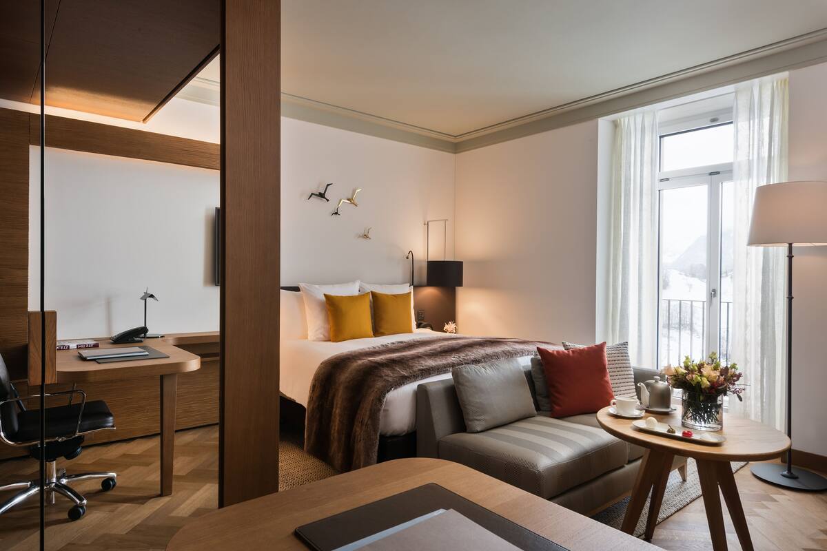 Quarto de hotel com cama, escrivaninha, sofá e uma pequena mesa com um vaso de flores.