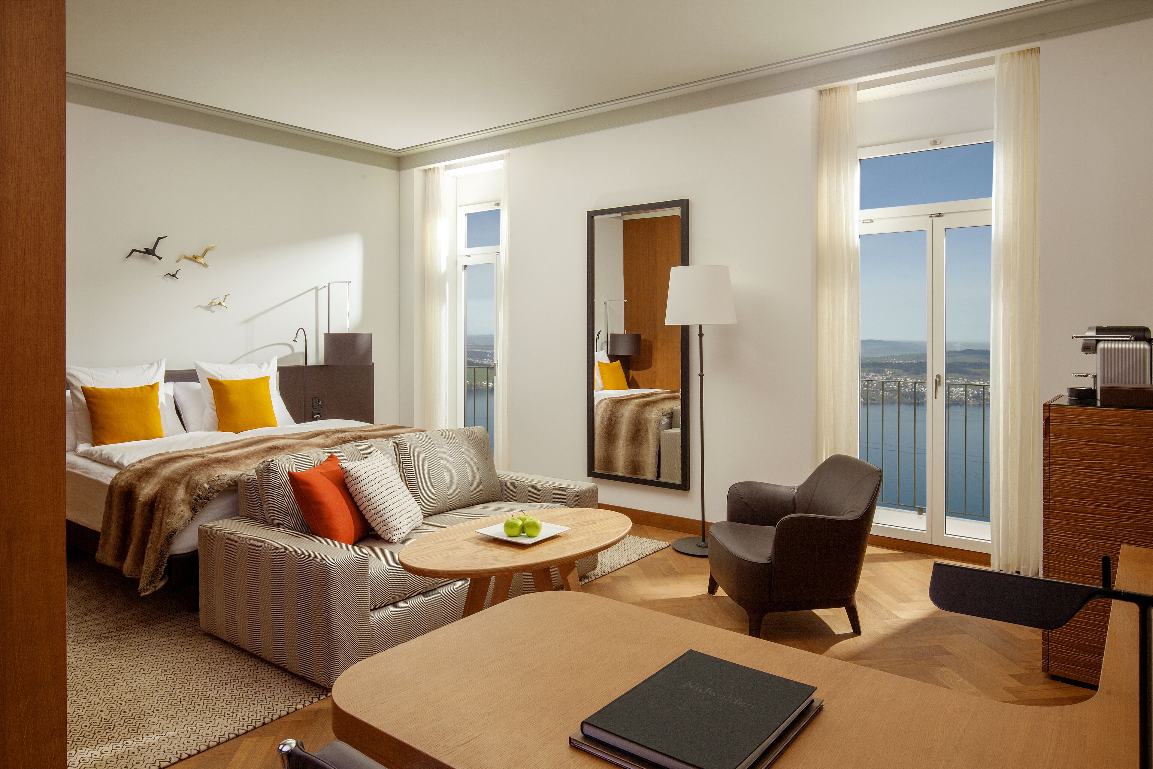 Una habitación de hotel moderna con cama, sofá, sillón y una mesa de comedor.
