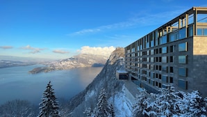 A modern building with a glass facade overlooking a snowy landscape and a body of water.