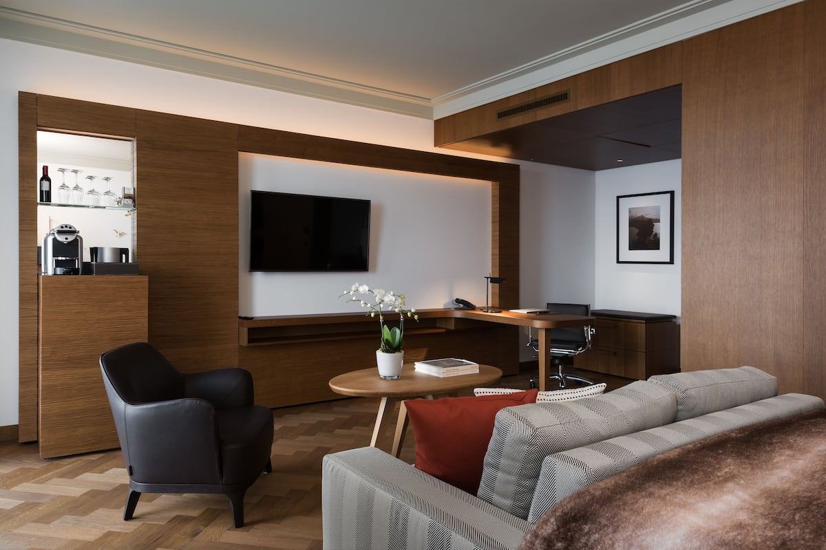 Uma sala de estar moderna com um sofá, uma poltrona, uma mesa de centro, uma TV e um armário de madeira com espaço para vinhos.
