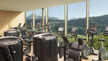 A gym with multiple exercise machines, large windows, and a view of mountains.