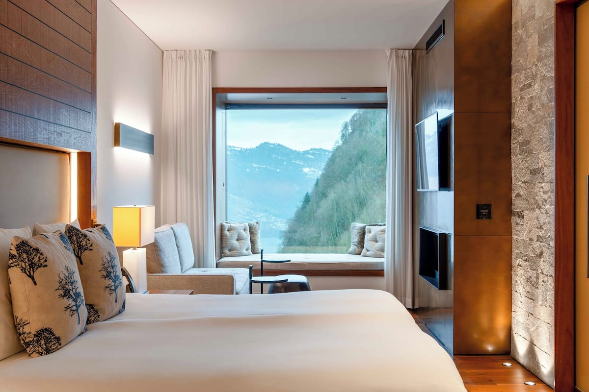 Quarto de hotel com uma cama grande, área de estar junto à janela e TV na parede.