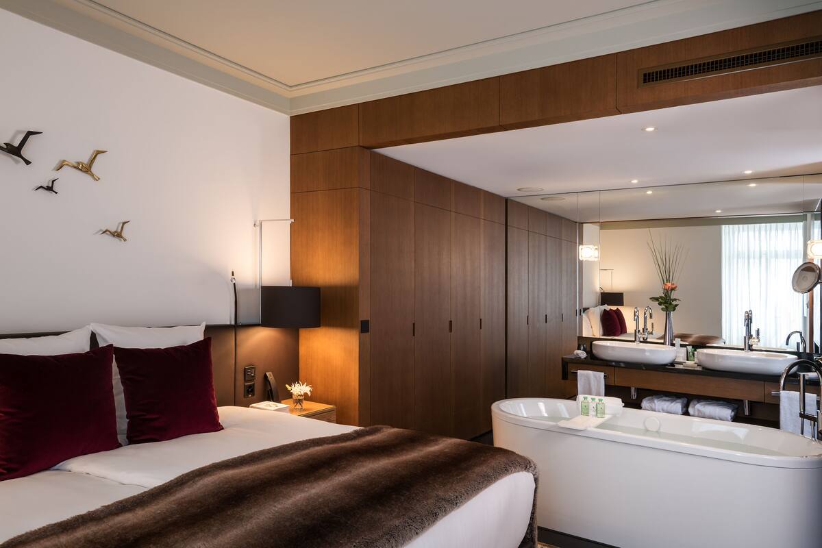 Quarto de hotel moderno com uma cama grande, banheiro com banheira e toucador com duas pias.