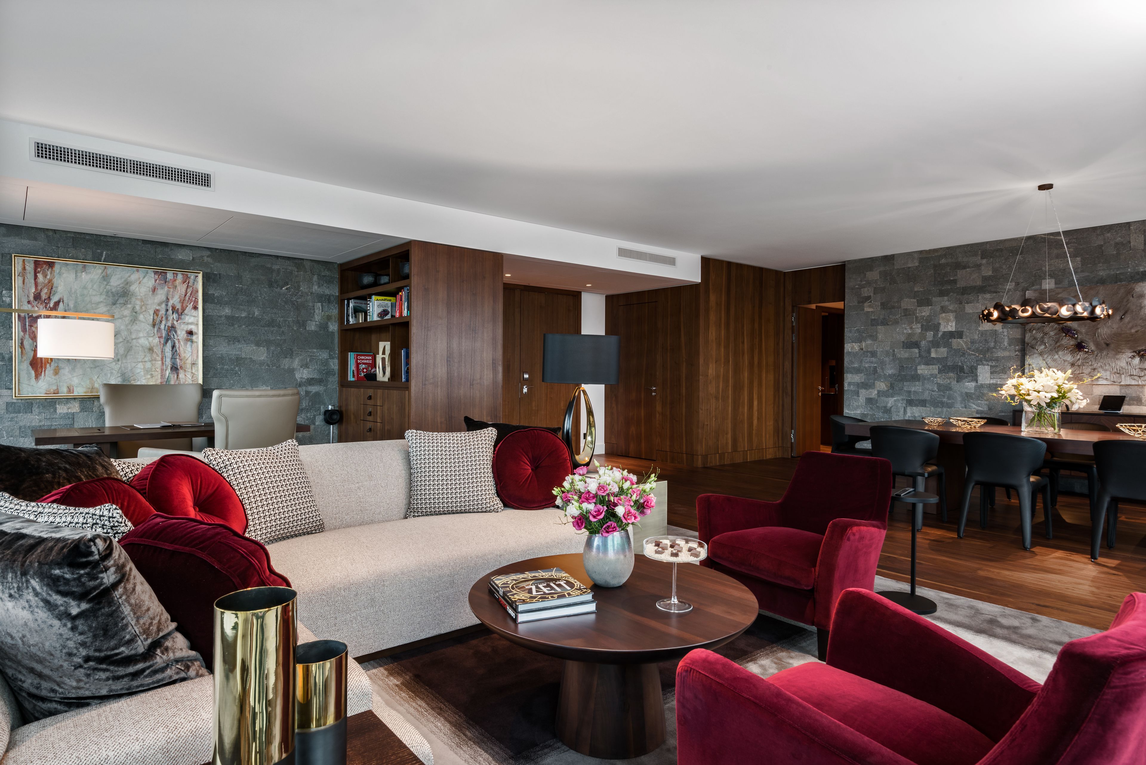 Una sala de estar moderna con un sofá, sillas rojas, una mesa de centro y un comedor con mesa y sillas.