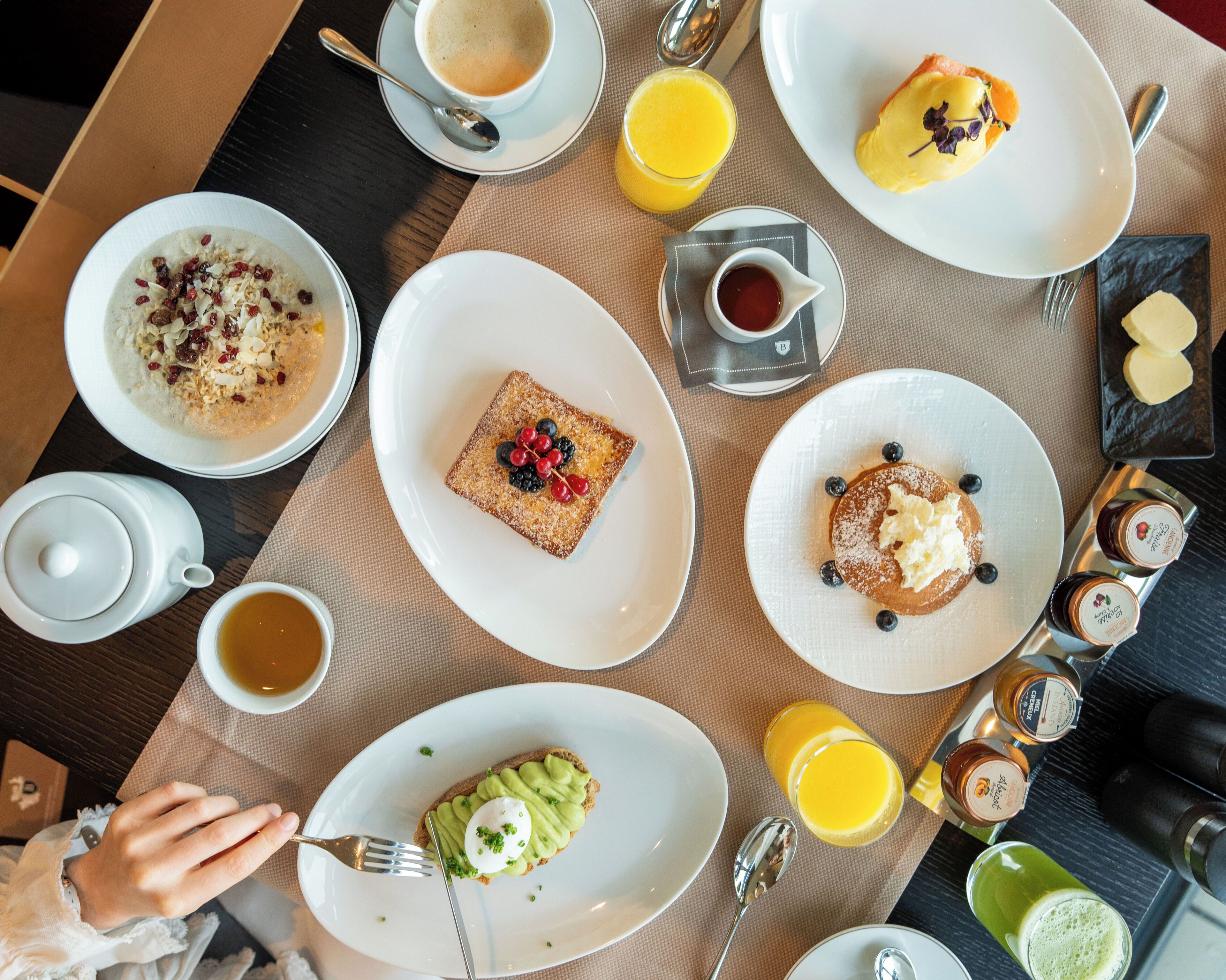 Een ontbijttafel met diverse gerechten, waaronder toast met bessen, pannenkoeken met bosbessen, en een glas sinaasappelsap.