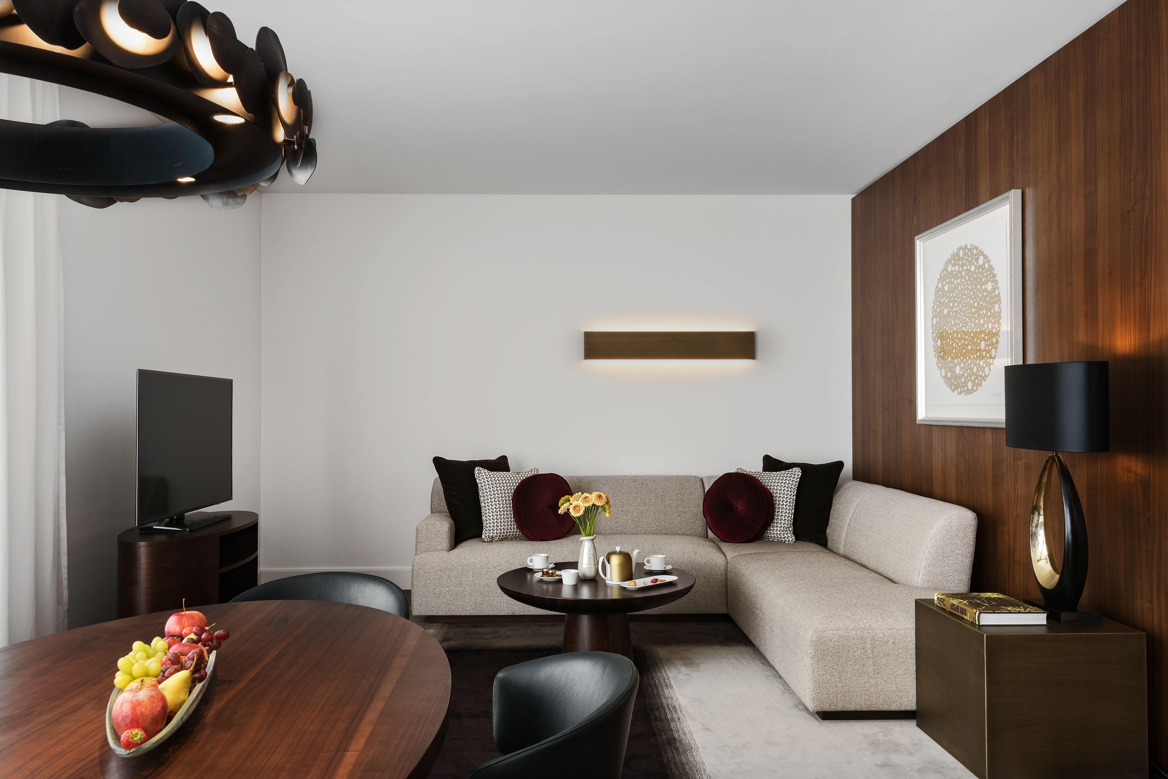 A modern living room with a sofa, a round coffee table with fruit, a TV, and a framed artwork on the wall.