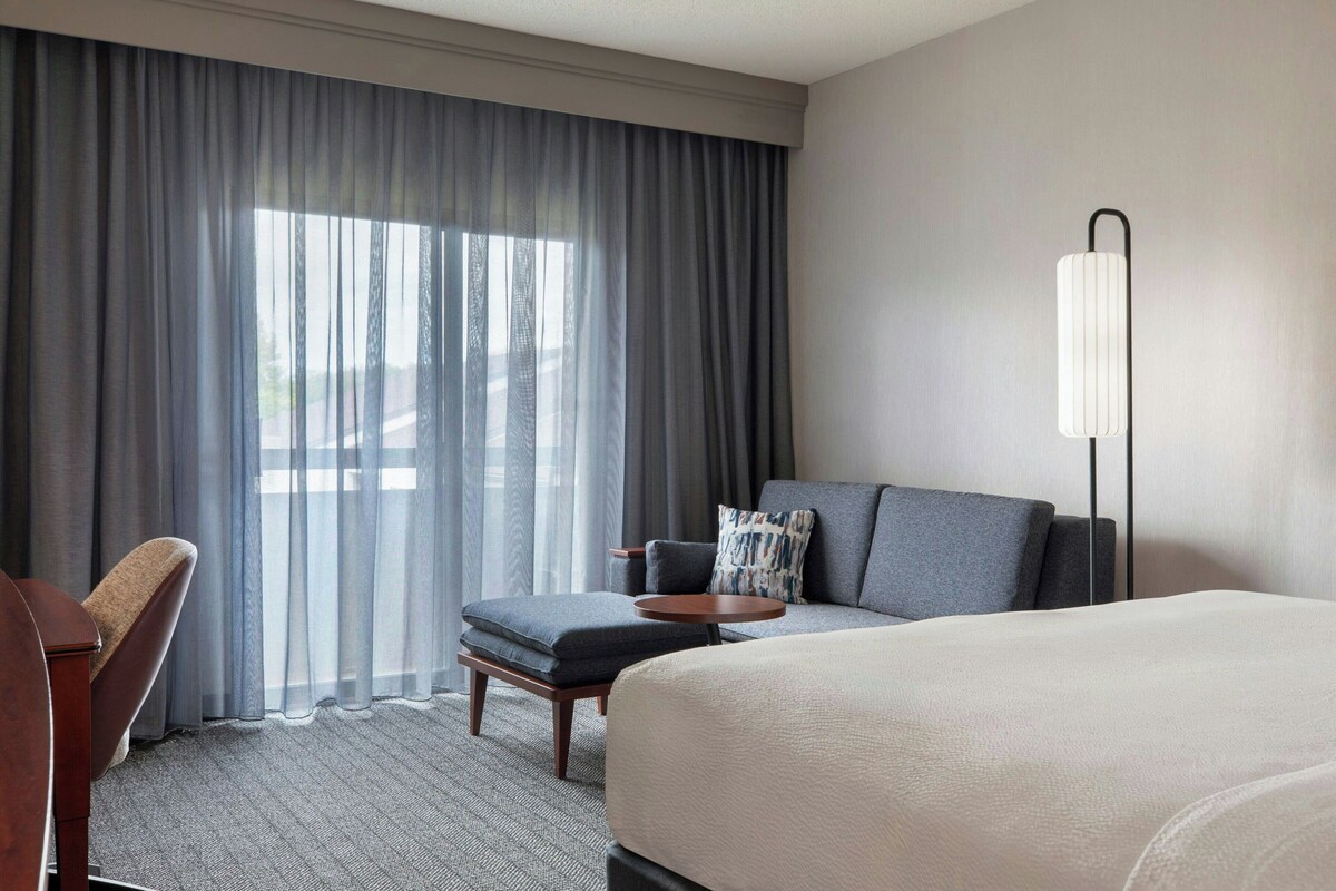 A hotel room with a bed, a sofa, a chair, a small table, and a lamp.