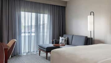A hotel room with a bed, a sofa, a chair, a small table, and a lamp.