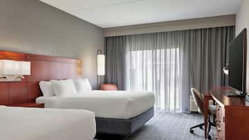 A hotel room with two beds, a desk, a chair, a TV, and a window with curtains.