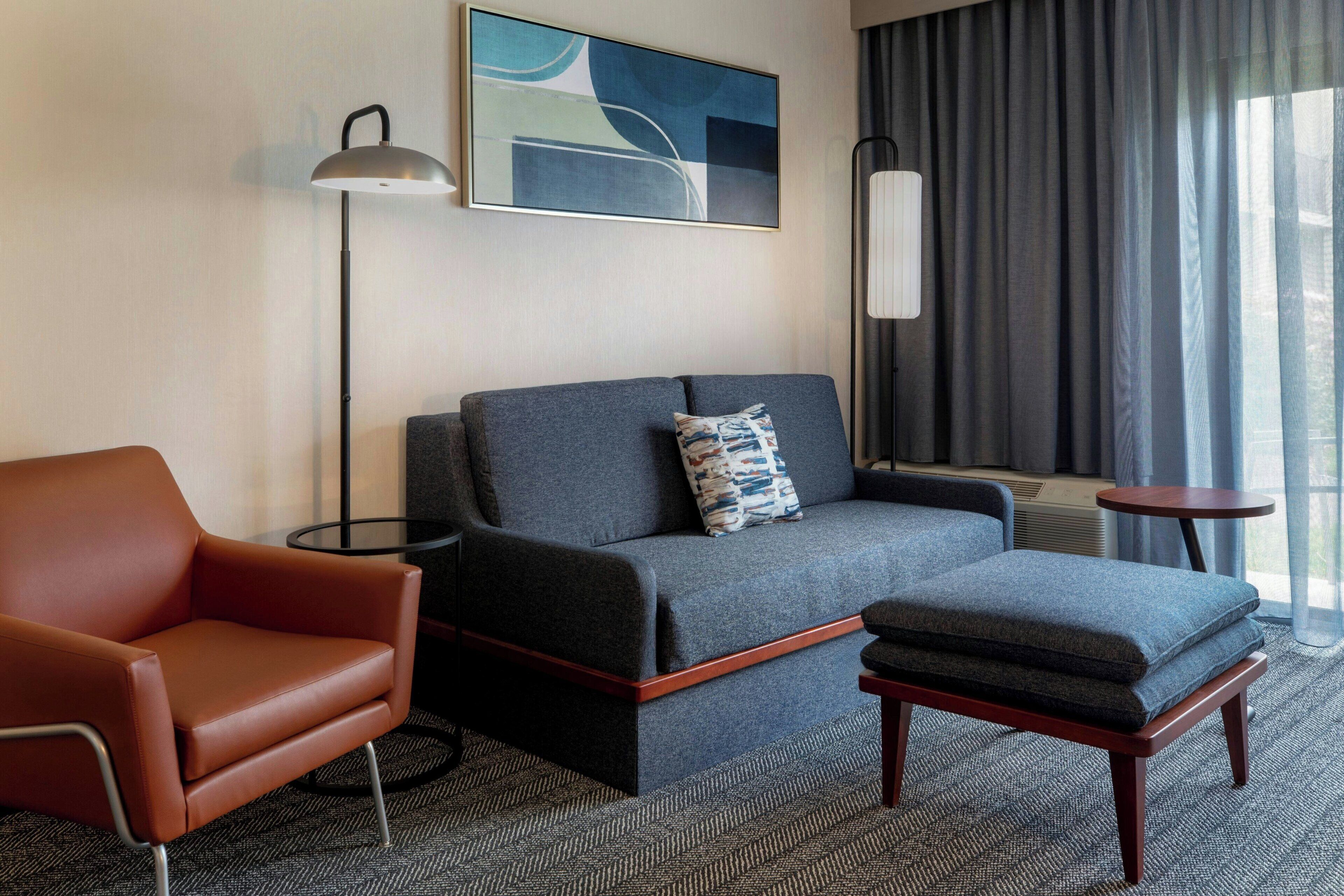 Una habitación de hotel moderna con sofá, sillón y una pequeña mesa.