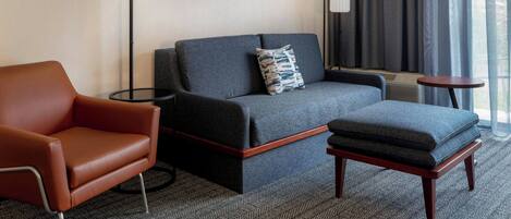 Una habitación de hotel moderna con sofá, sillón y una pequeña mesa.