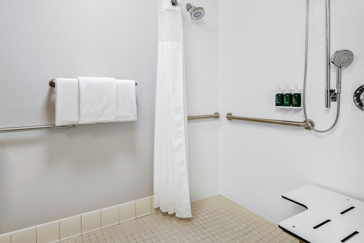 Ein Badezimmer mit weißer Dusche, Handtuchhalter, Haltegriff und Ablagefläche für Toilettenartikel.