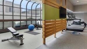 Una sala de gimnàstica amb equip d'exercici, una banca, una pilota i una pantalla de televisió.